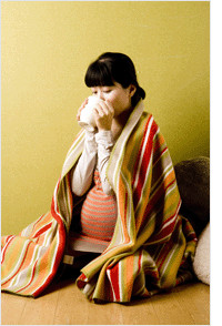 담요를 덮고 앉아서 음료를 마시는 임산부